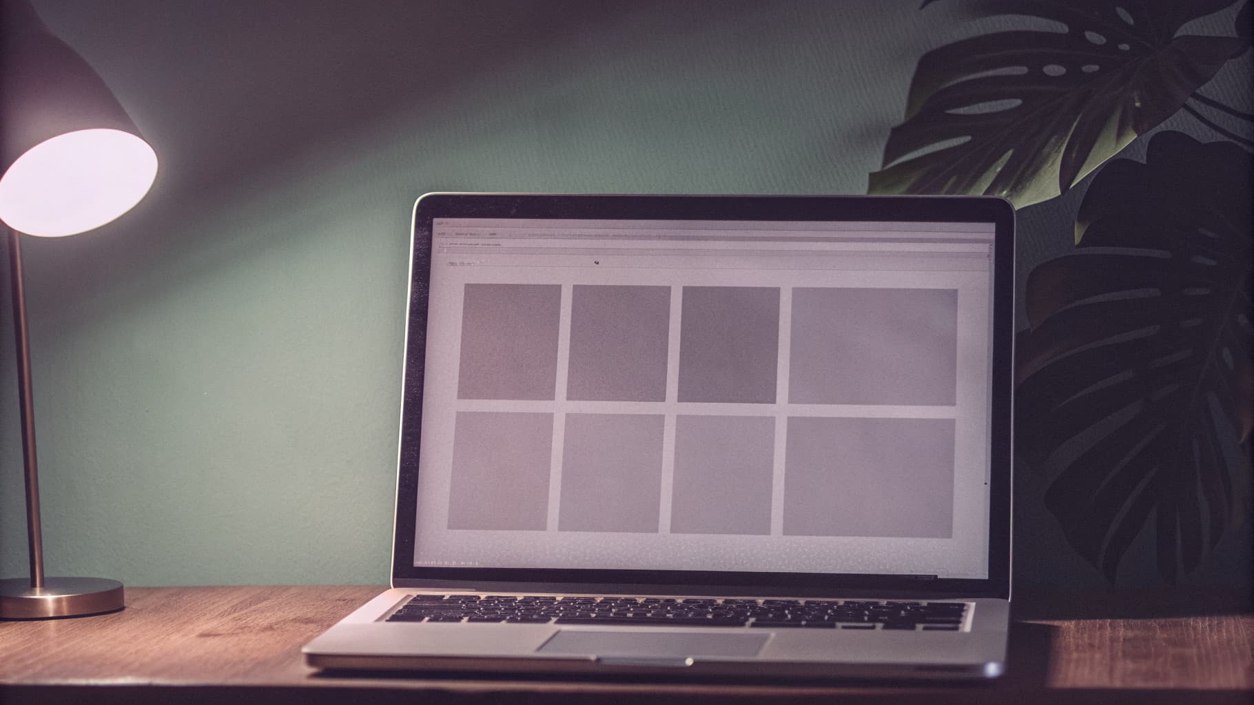 A laptop on a warm wood desk showing a simple, clean website layout, with tropical leaf shadows and a mint-green accent light